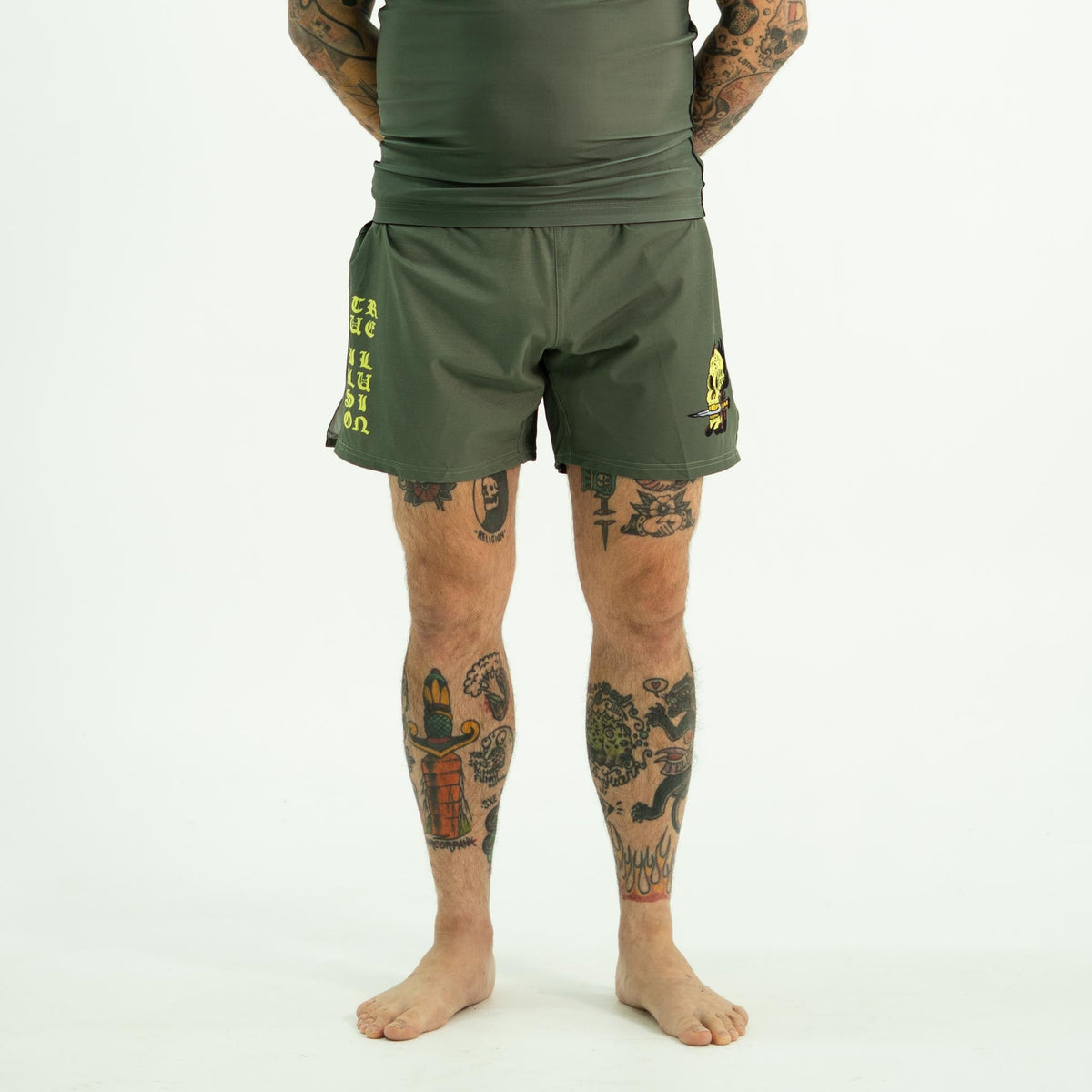 True Illusion Fire Skull Shorts, front view worn, olive green with yellow gothic text on left leg and skull graphic on right