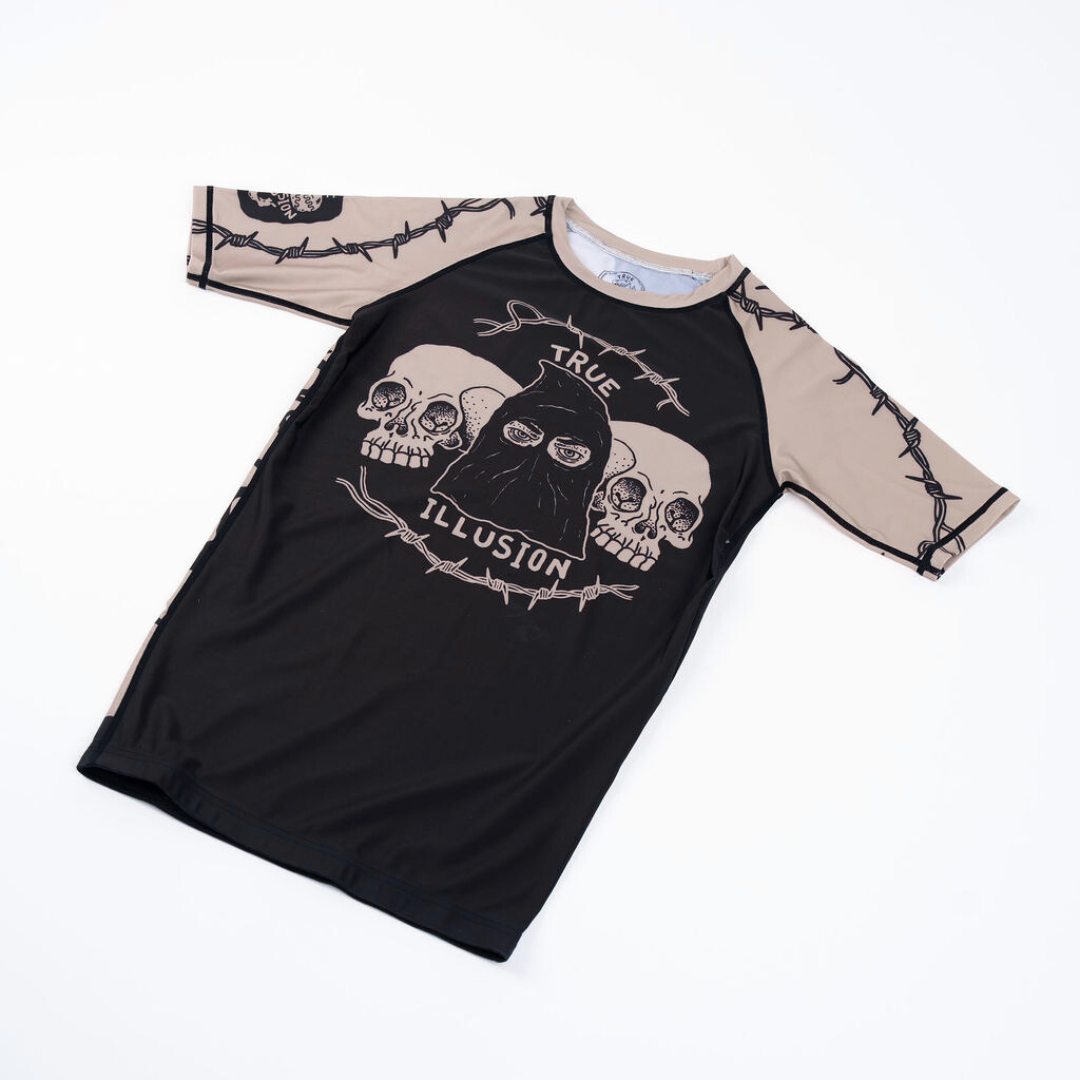 True Illusion Executioner Short Sleeve BJJ Rash Guard, front flat lay showing skull graphic and barbed wire print on tan