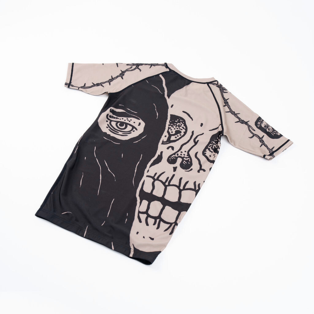 True Illusion Executioner Short Sleeve BJJ Rash Guard, front flat lay showing split skull graphic in black and tan